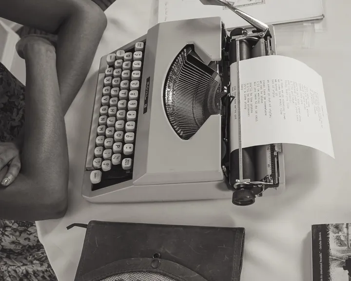 Person Sitting At A Table With An Old Typewriter Where They Have Almost A Page Written